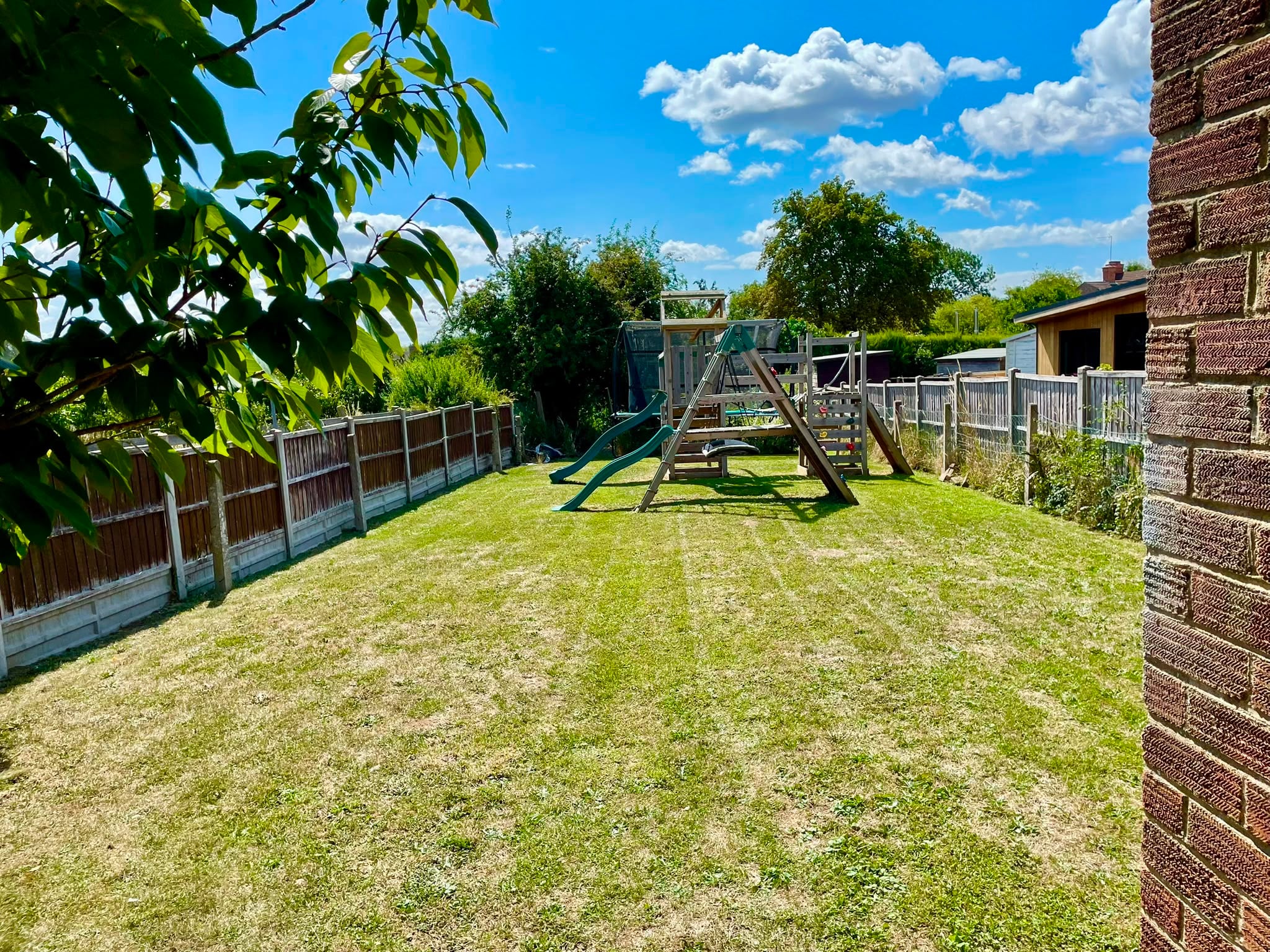 The same garden mown short and level right up to the fence line, with the climbing frame and lawn usable again