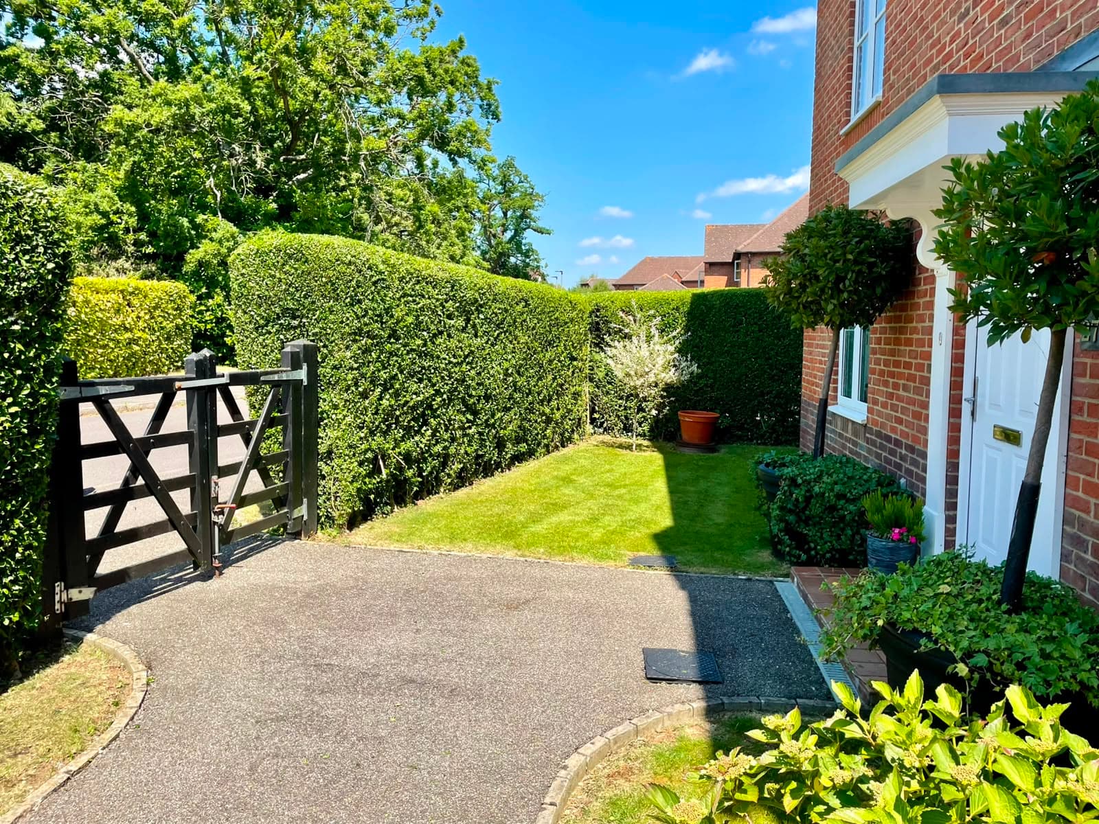 A neatly clipped front hedge and mown lawn beside a five-bar gate and a house entrance